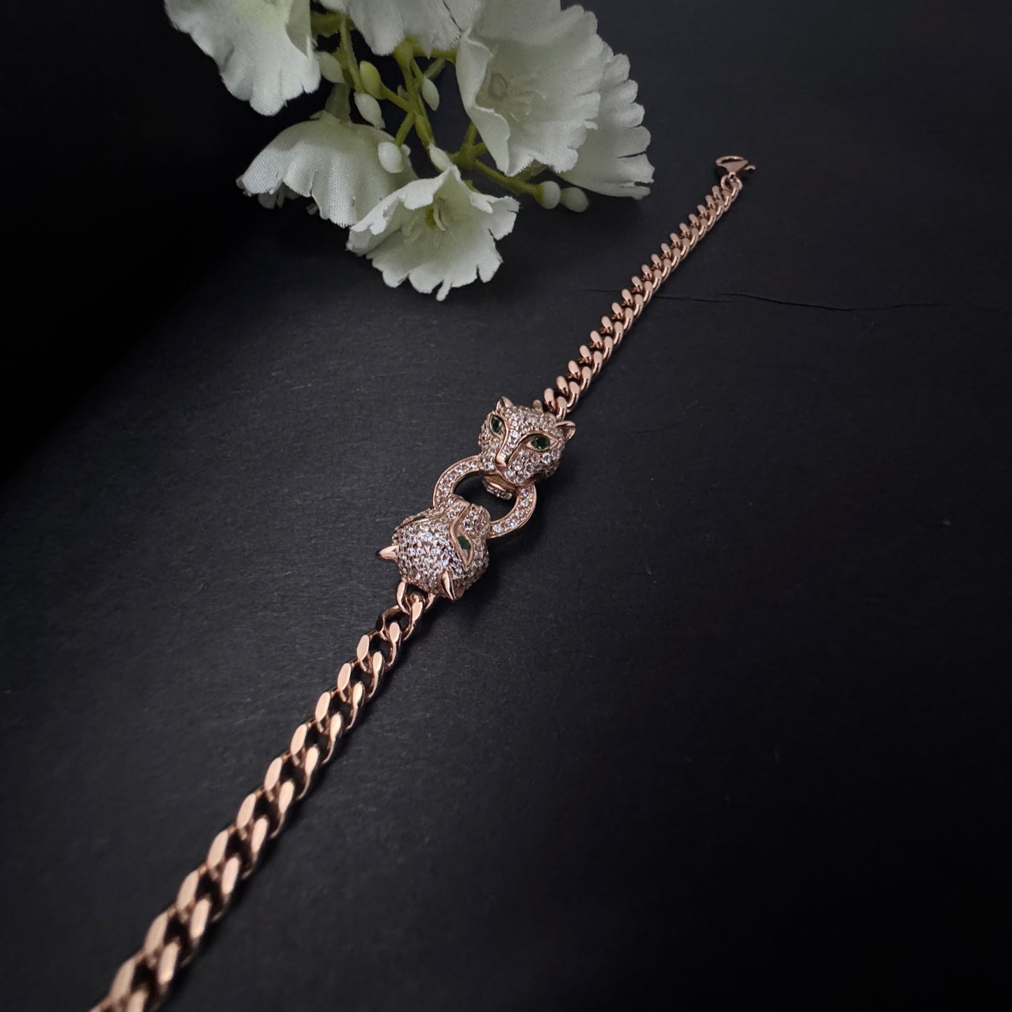 Rose gold bracelet with intricate design on a dark surface with white flowers.