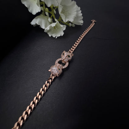 Rose gold bracelet with intricate design on a dark surface with white flowers.