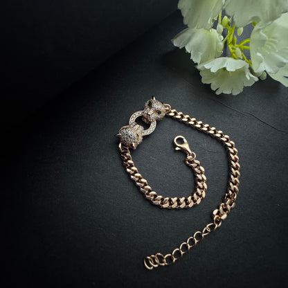 Gold chain bracelet with clasp on a dark surface with light green flowers.