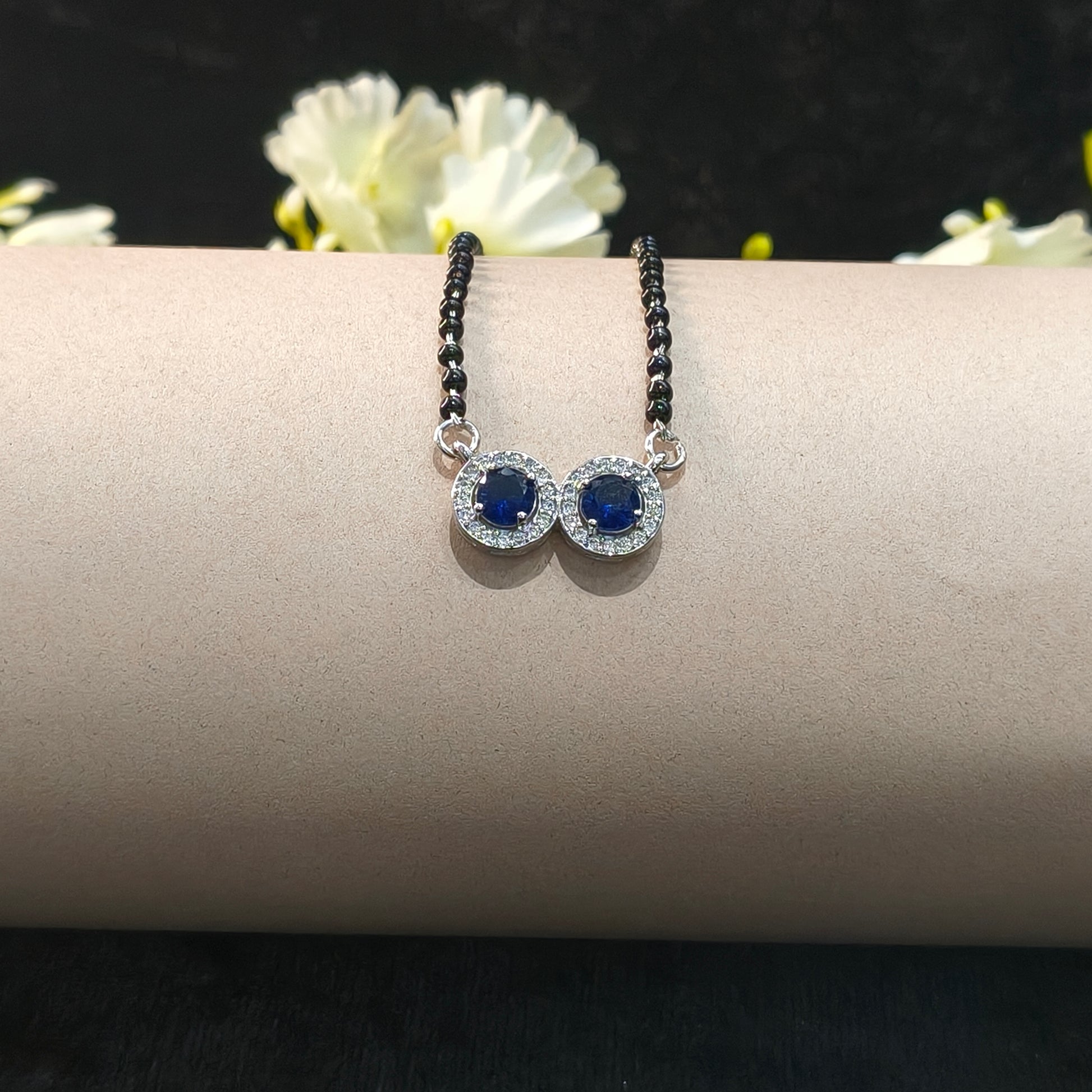 Pair of earrings with blue gemstones on a beige stand with flowers in the background