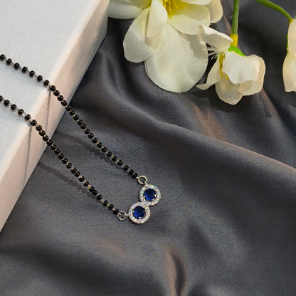 Necklace with blue gemstones on a dark fabric background with white flowers.