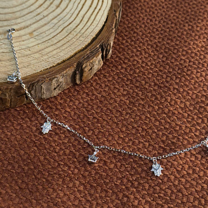 Silver necklace with star-shaped pendants on a brown textured surface with a wooden log.