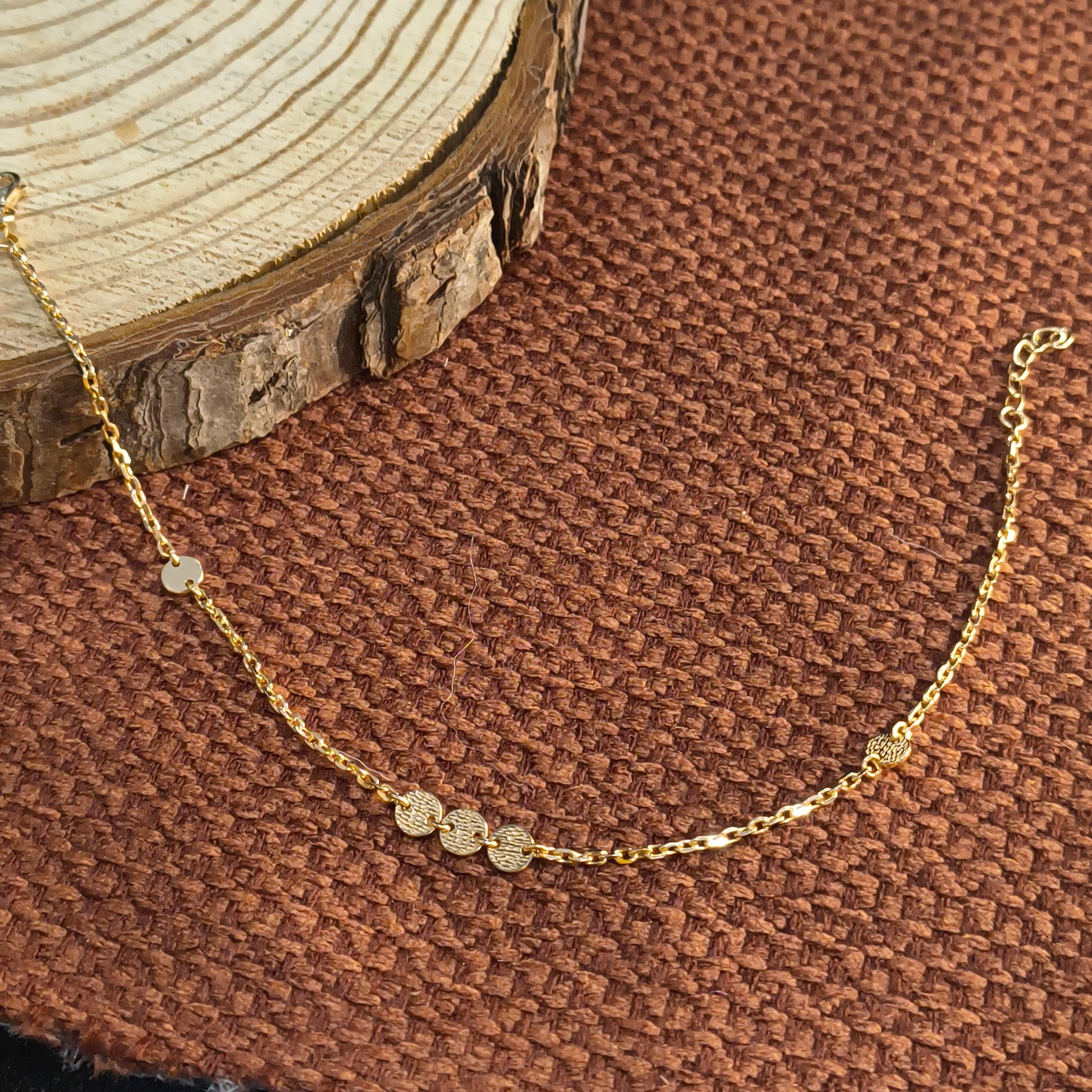 Gold necklace with circular pendants on a brown textured fabric background