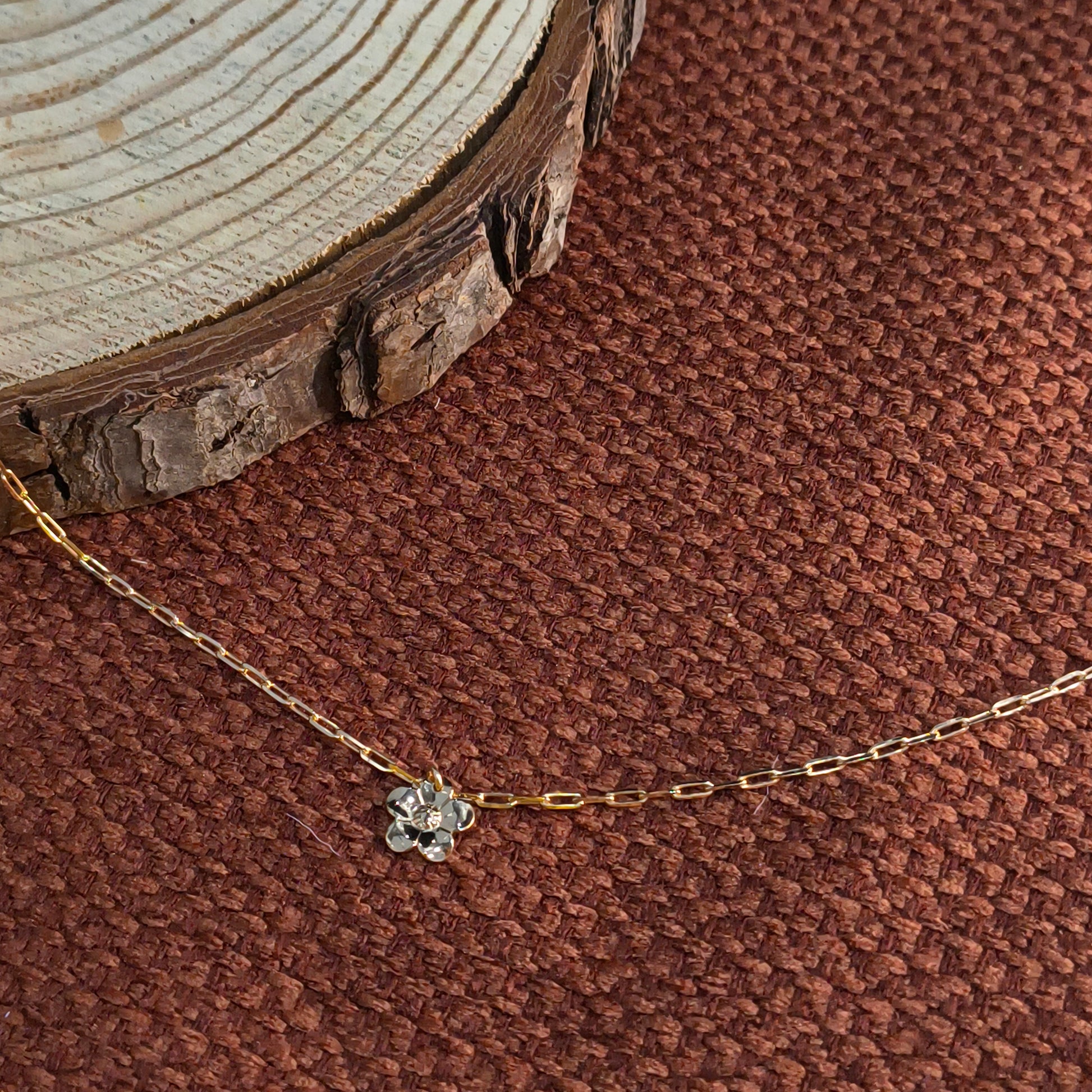 Gold necklace with a floral pendant on a brown textured background