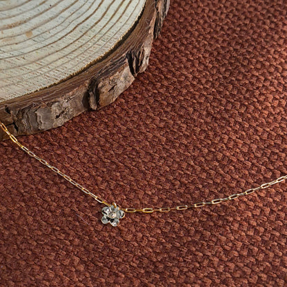 Gold necklace with a floral pendant on a brown textured background