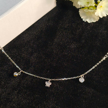 Silver necklace with floral pendants on a black surface with white flowers.