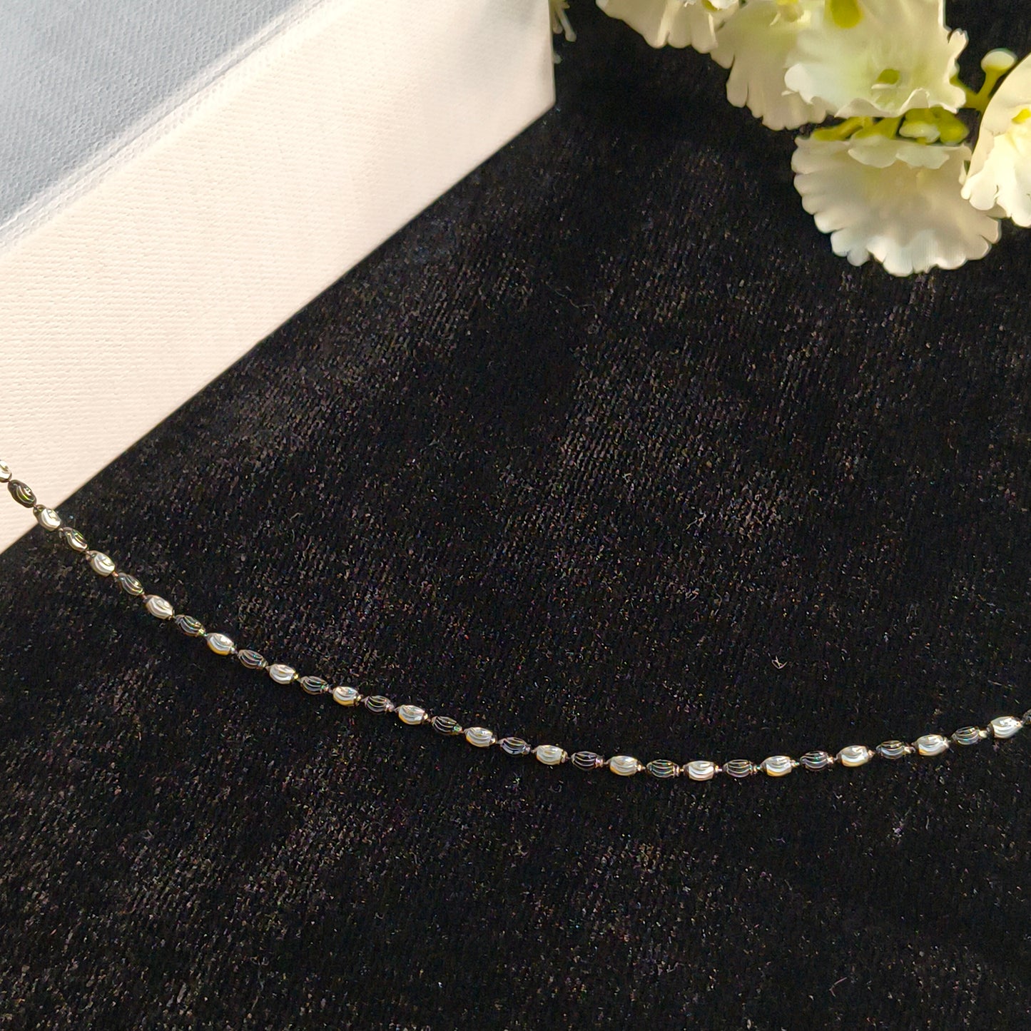 Necklace on a black surface with white flowers in the corner