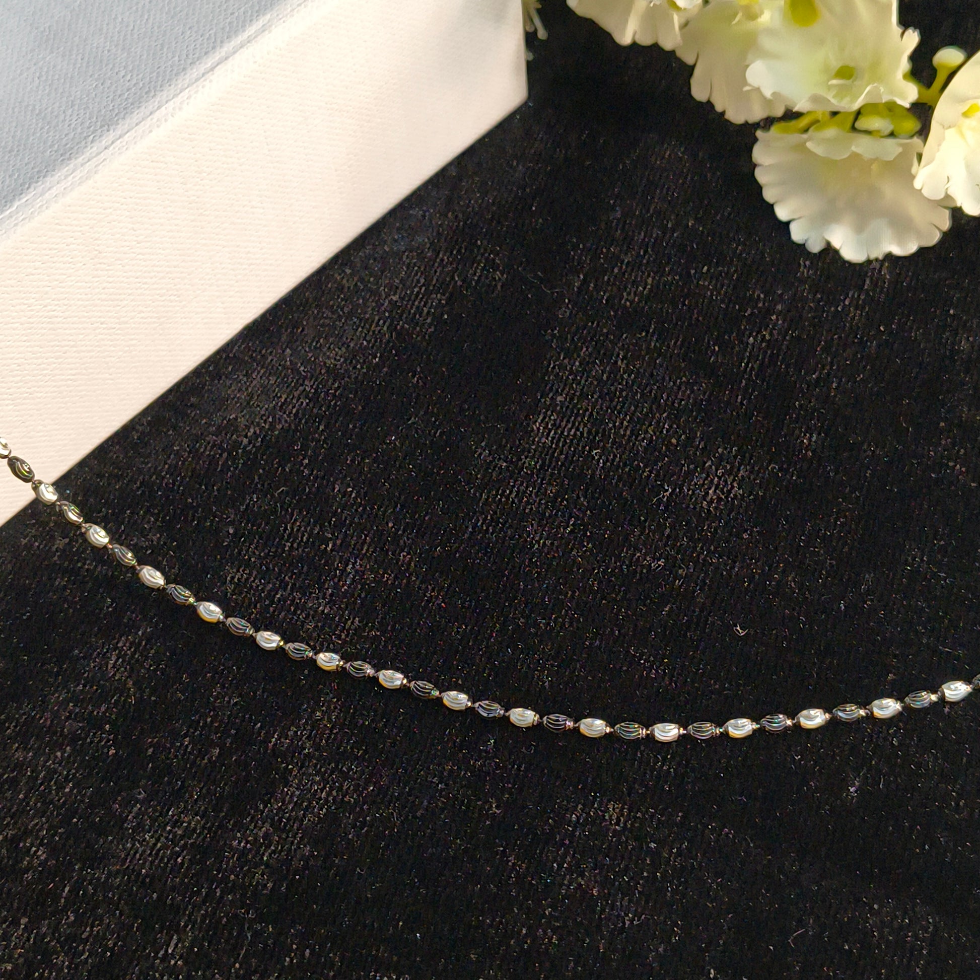 Necklace on a black surface with white flowers in the corner