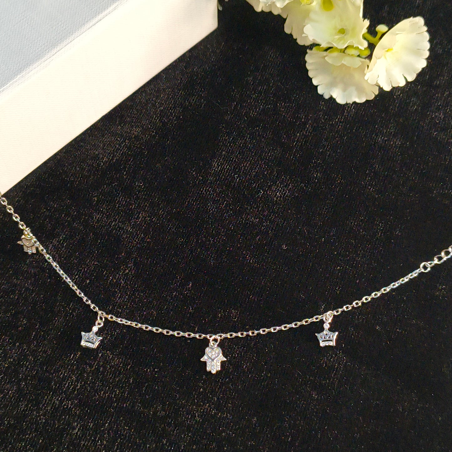 Silver necklace with charms on a black surface with white flowers