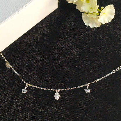 Silver necklace with charms on a black surface with white flowers