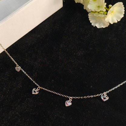 Necklace with heart-shaped pendants on a black surface with white flowers.