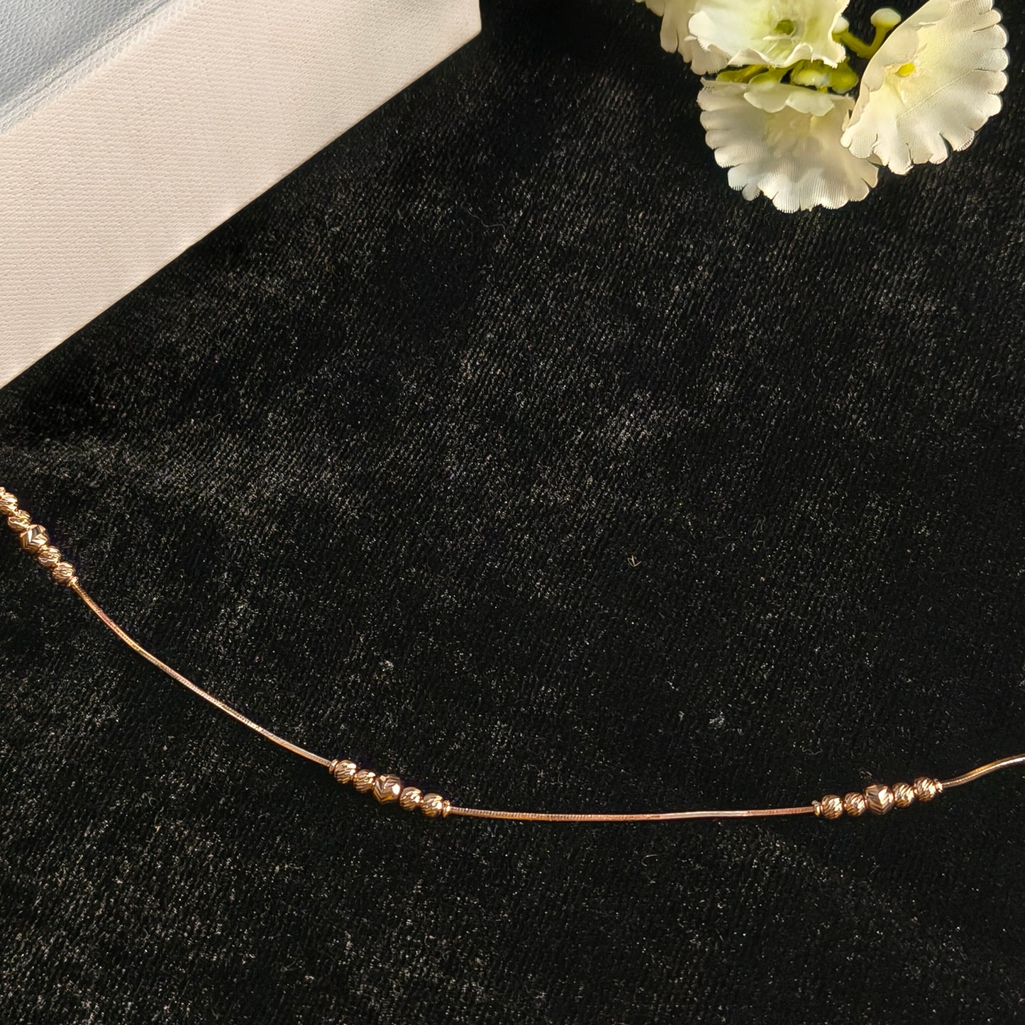 Delicate gold necklace on a black surface with white flowers