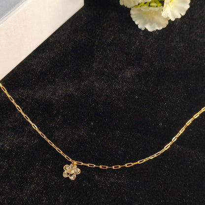 Gold chain necklace with a floral pendant on a black surface with white flowers.