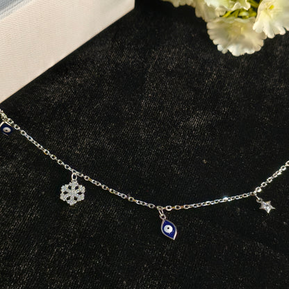 Silver bracelet with eye and flower charms on a black surface with white flowers.