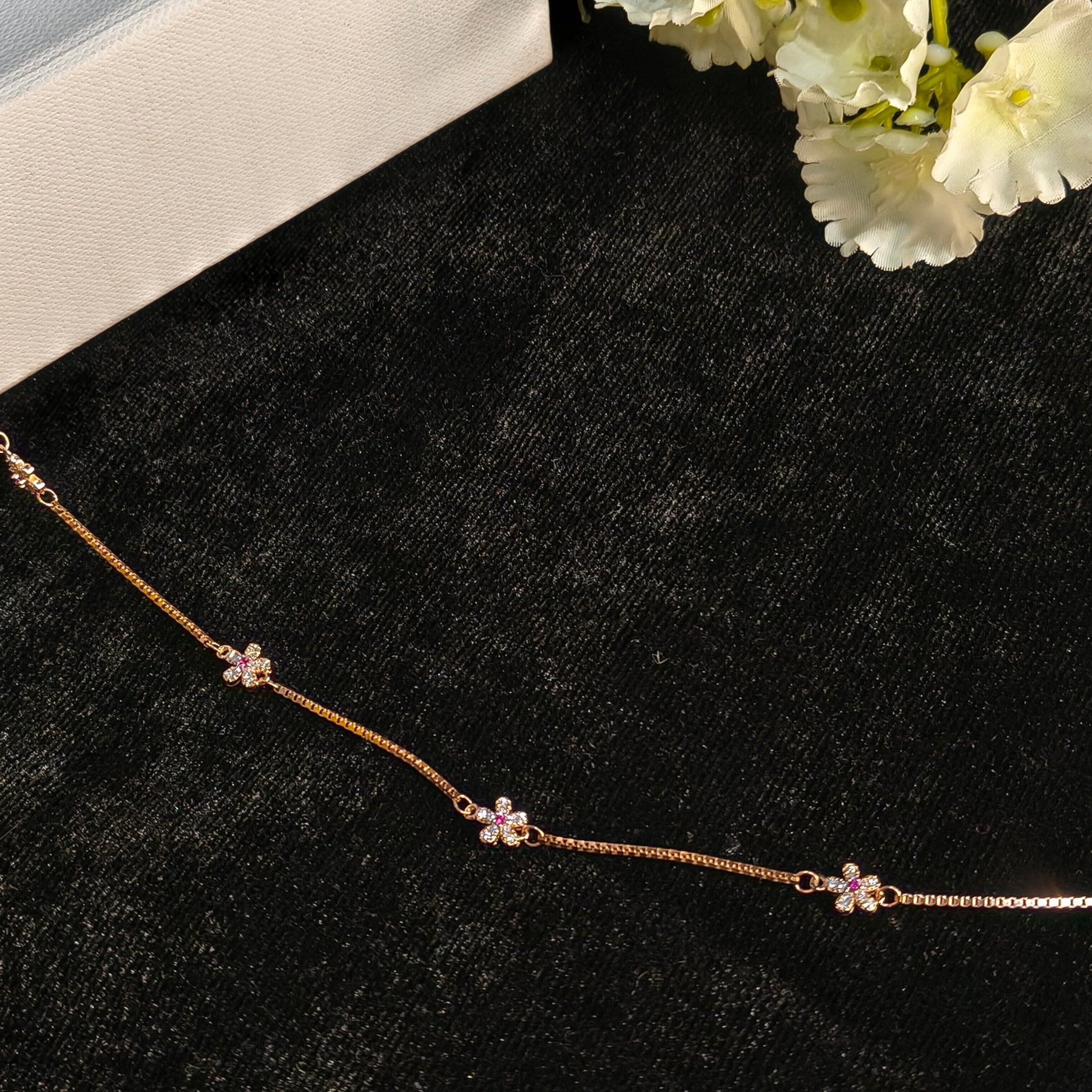 Rose gold necklace with floral designs on a black surface with white flowers.