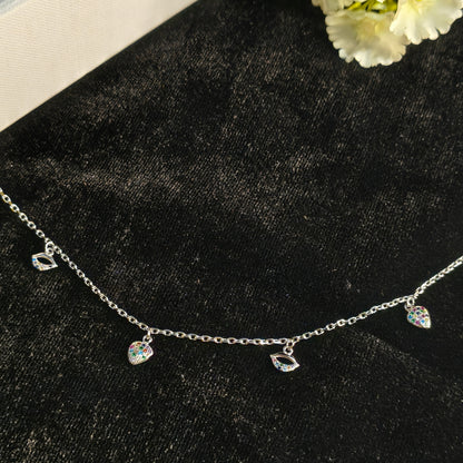 Delicate silver necklace with heart-shaped charms on a black surface with white flowers.