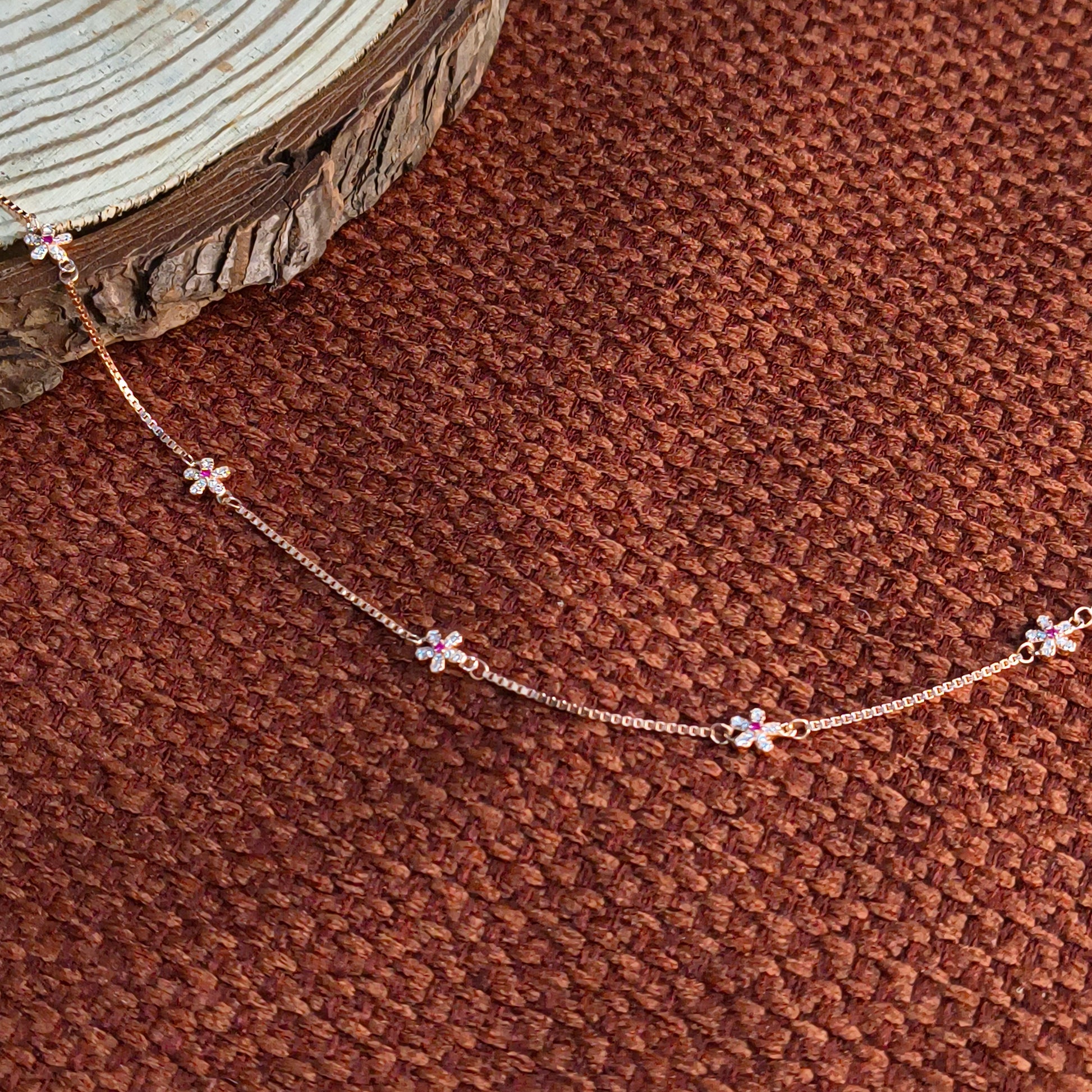 Delicate gold necklace with floral pendants on a brown textured surface