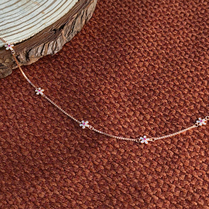 Delicate gold necklace with floral pendants on a brown textured surface