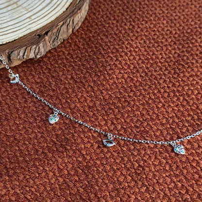 Silver necklace with heart-shaped pendants on a brown textured surface