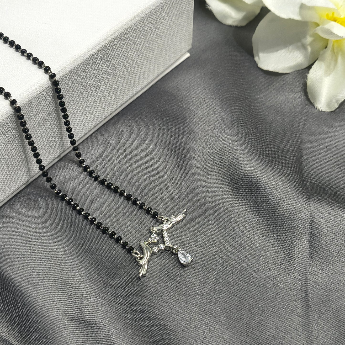 Necklace with black beads and silver pendant on a gray surface with white flowers.