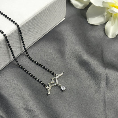 Necklace with black beads and silver pendant on a gray surface with white flowers.