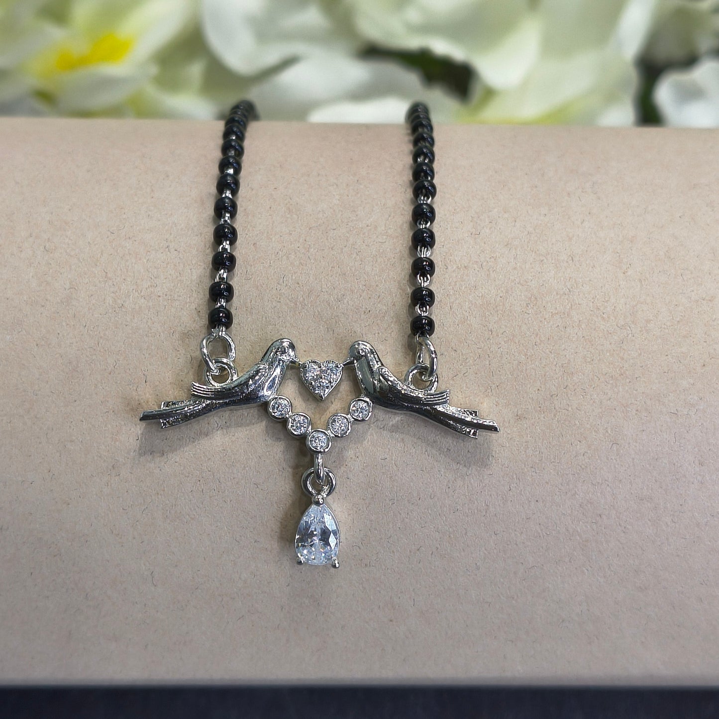 Bracelet with black beaded chain, silver high heel shoes, and a teardrop-shaped pendant on a beige surface.