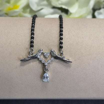 Bracelet with black beaded chain, silver high heel shoes, and a teardrop-shaped pendant on a beige surface.