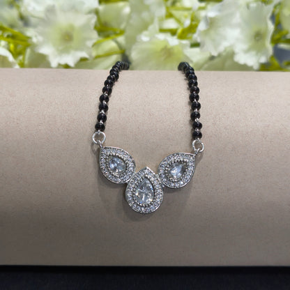 Silver bracelet with teardrop-shaped stones on a gray surface with flowers in the background