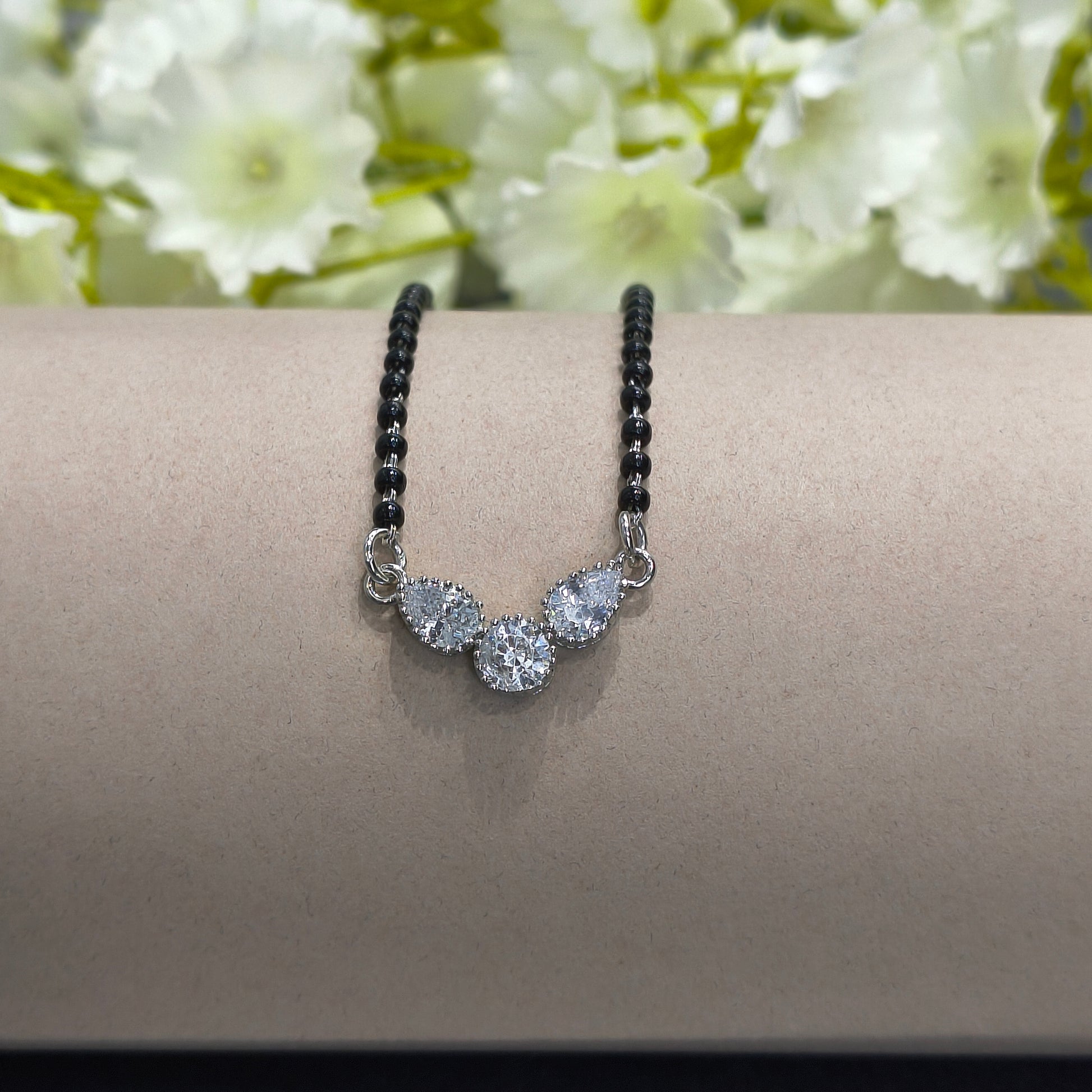 Bracelet with black beads and silver floral charm on a wrist against a floral background