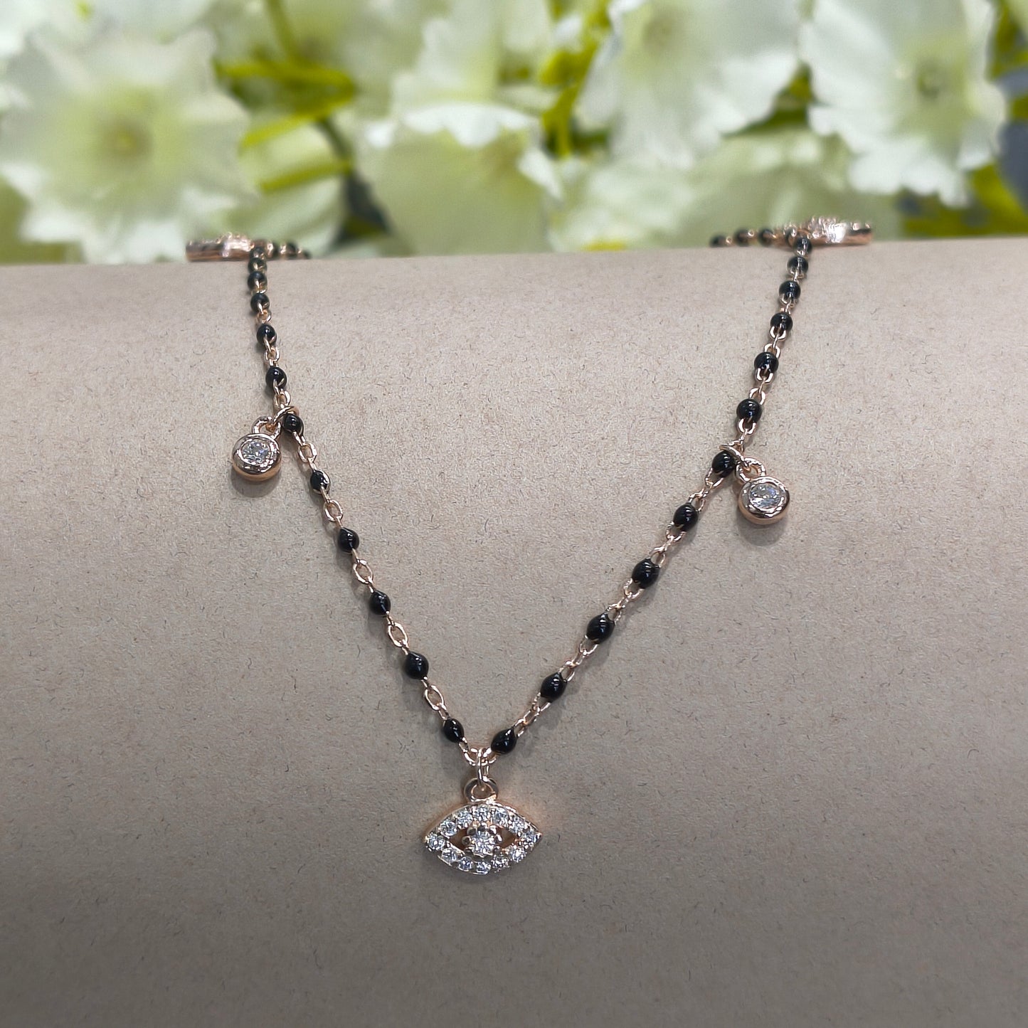 Delicate bracelet with black beads and silver charms on a gray stand with white flowers in the background