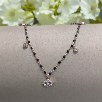 Delicate bracelet with black beads and silver charms on a gray stand with white flowers in the background
