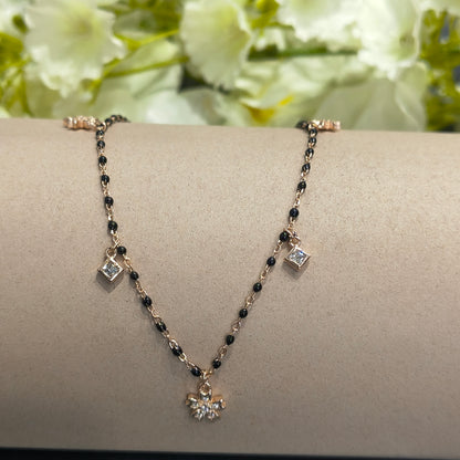 Gold bracelet with black beads and silver charms on a neutral background