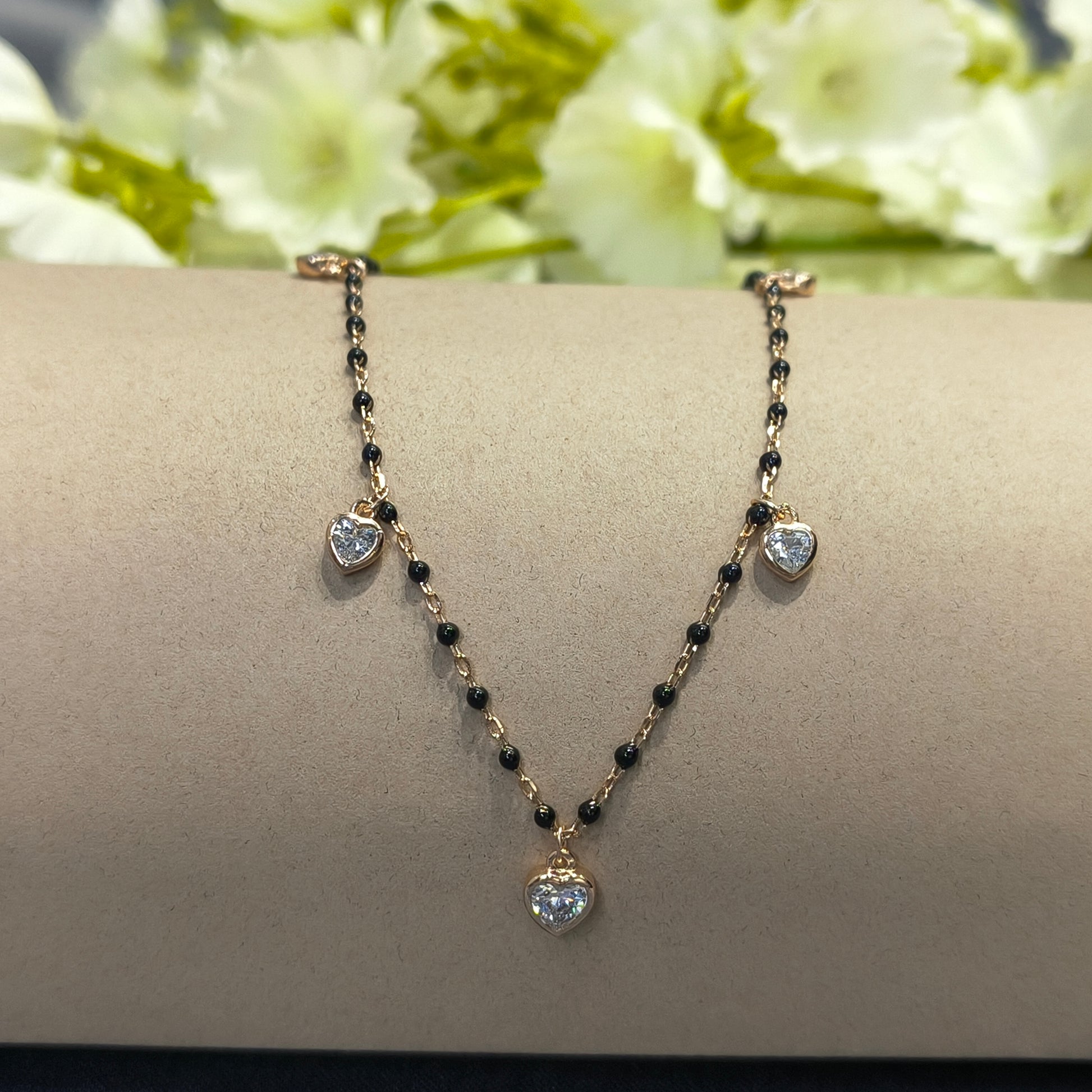 Gold bracelet with heart-shaped gemstones on a neutral background with flowers.