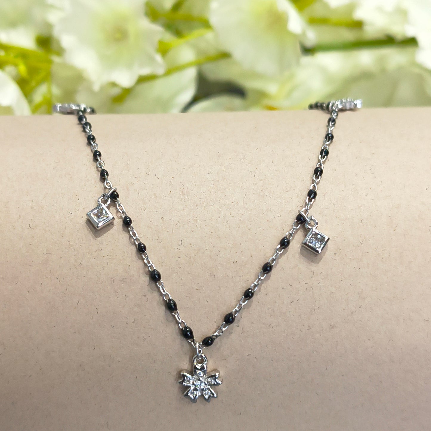 Silver anklet with black beads on a mannequin leg against a floral background
