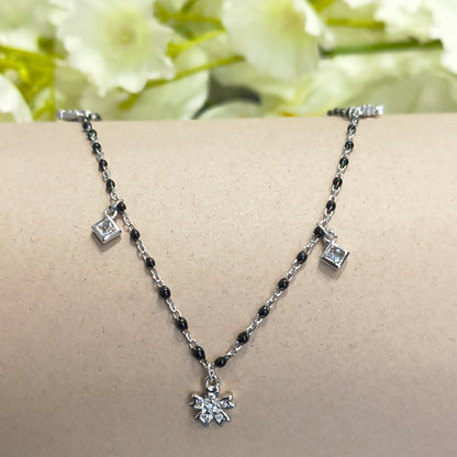 Silver anklet with black beads on a mannequin leg against a floral background