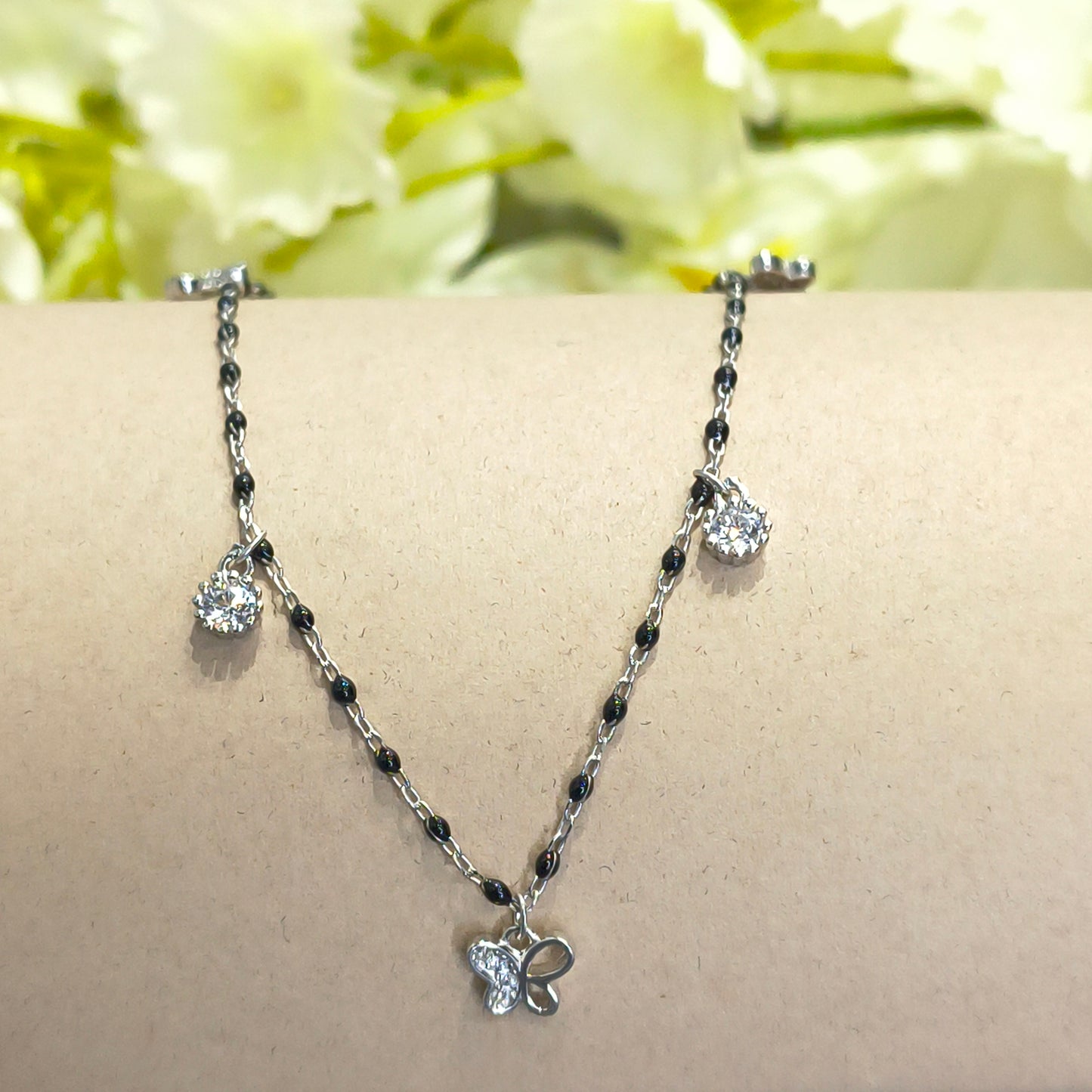 Silver bracelet with black beads on a mannequin arm against a floral background
