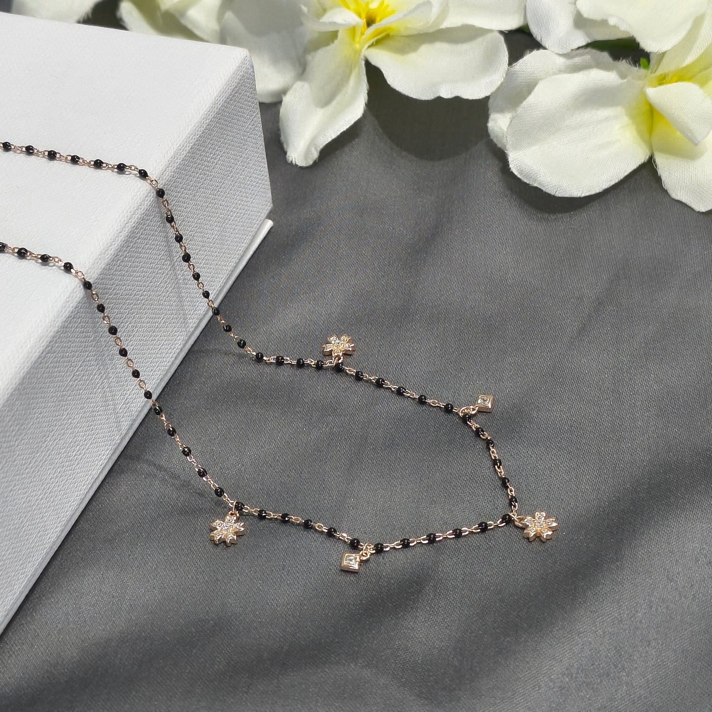 Necklace with floral pendants on a gray surface with white flowers in the background