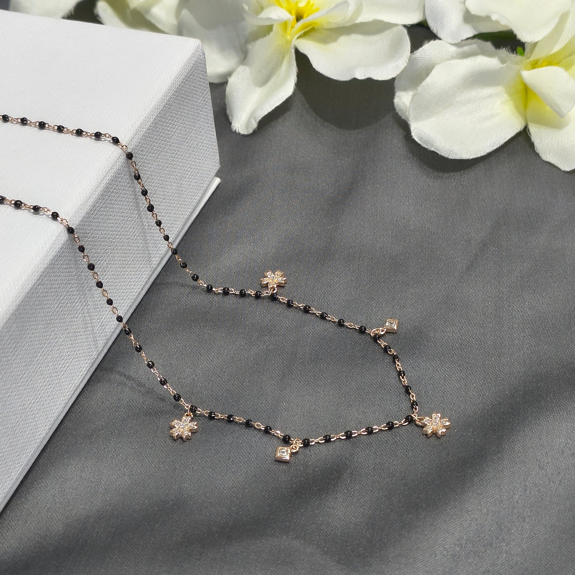 Necklace with floral pendants on a gray surface with white flowers in the background
