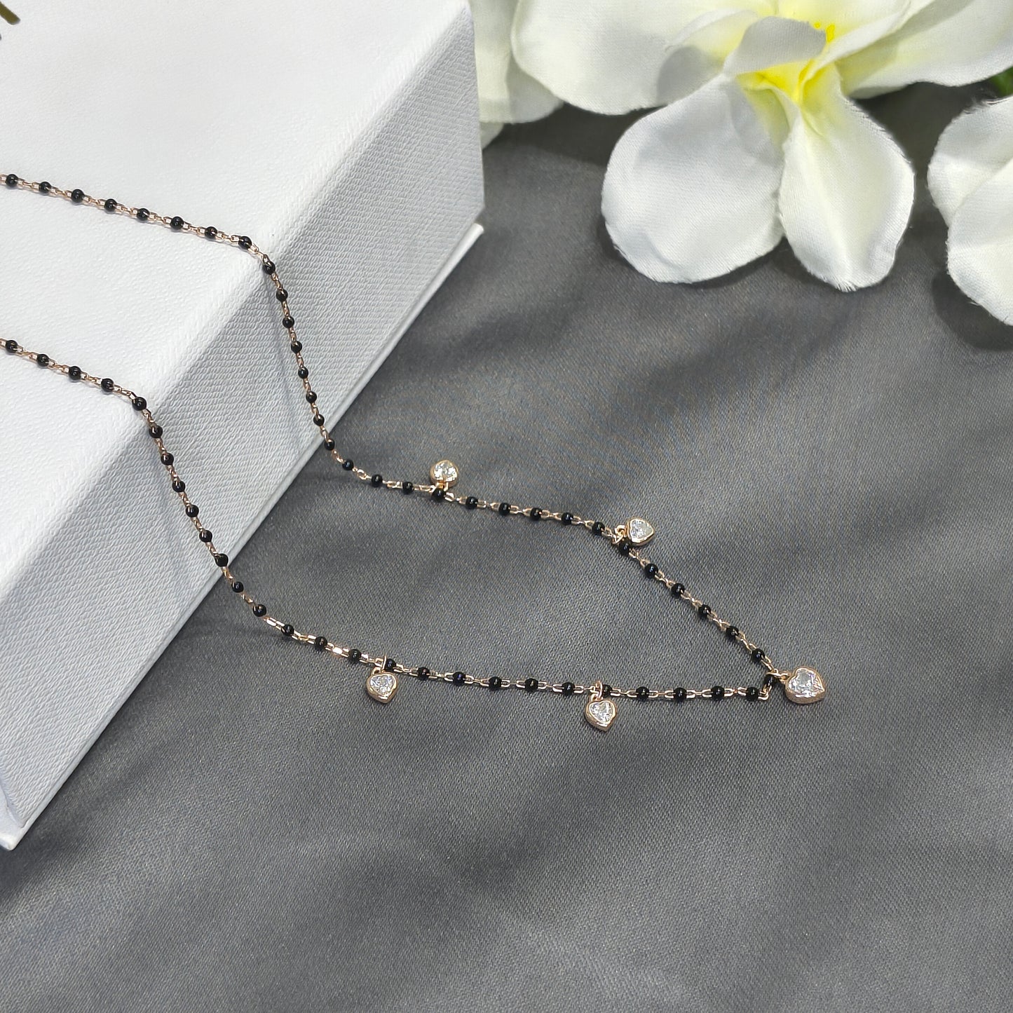 Delicate black beaded necklace on a gray surface with white flowers in the background