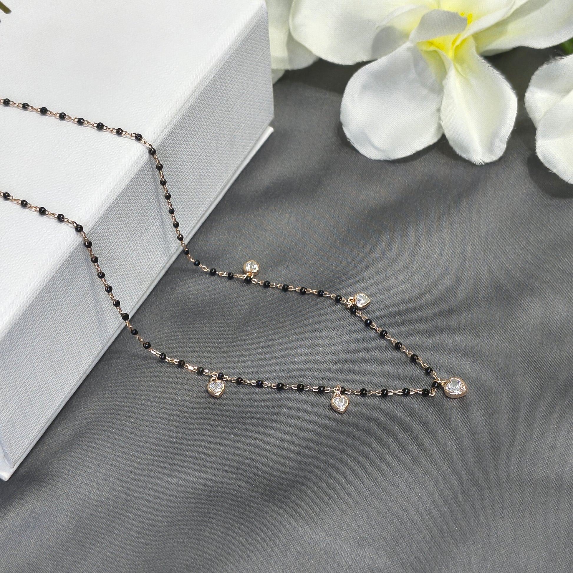 Delicate black beaded necklace on a gray surface with white flowers in the background