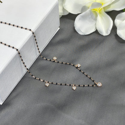 Delicate black beaded necklace on a gray surface with white flowers in the background