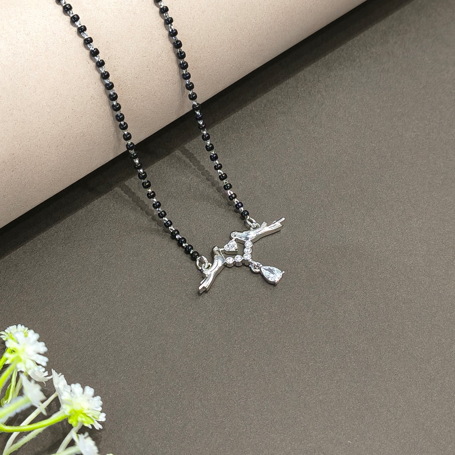 Necklace with a bird pendant on a dark surface with flowers in the corner