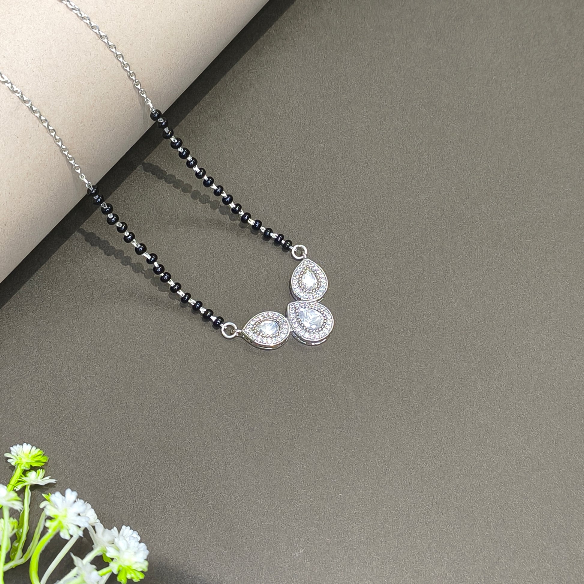 Necklace with black beads and silver pendants on a gray surface with a white flower.
