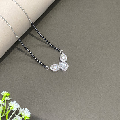 Necklace with black beads and silver pendants on a gray surface with a white flower.