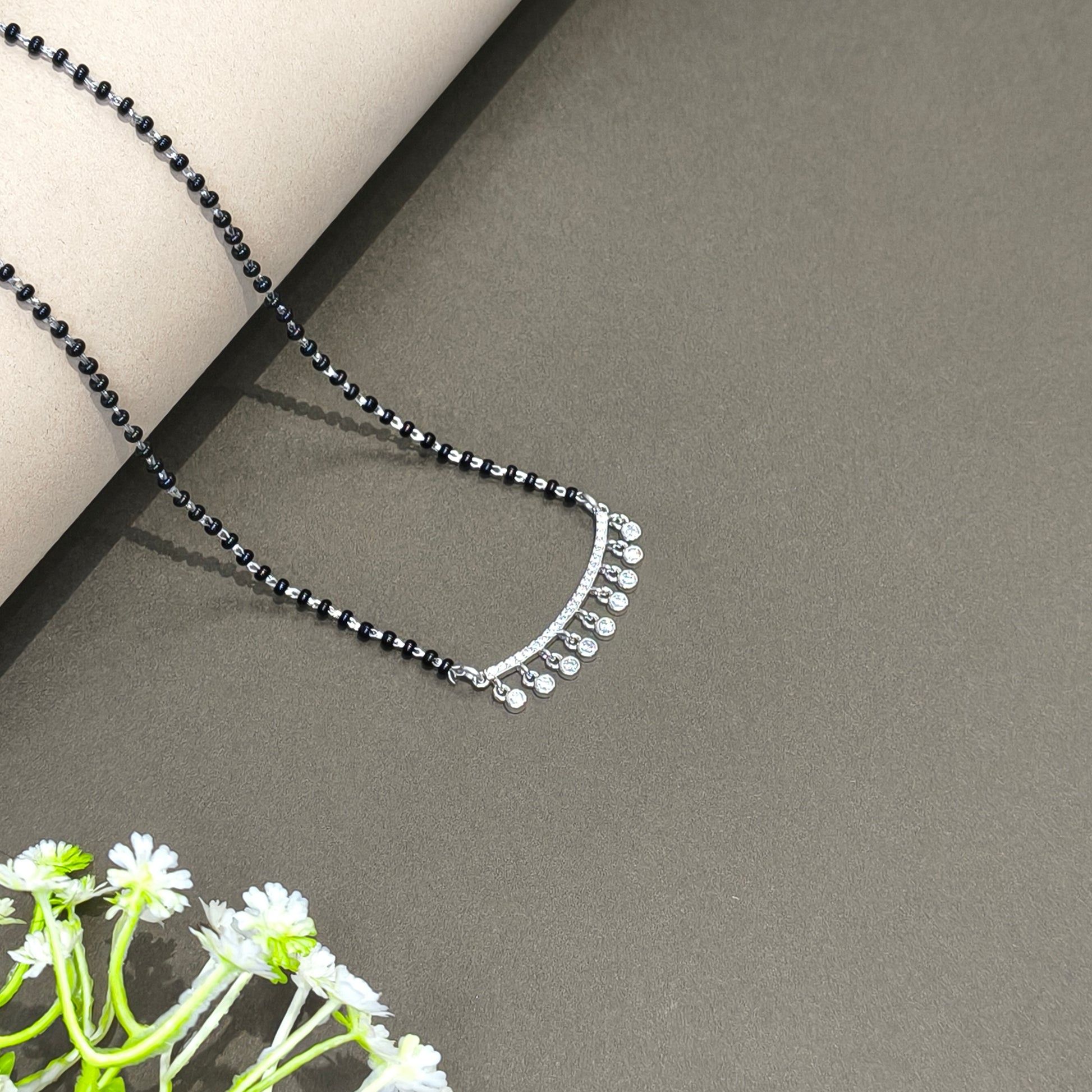 Black beaded necklace with silver clasp on a gray surface with a plant in the corner