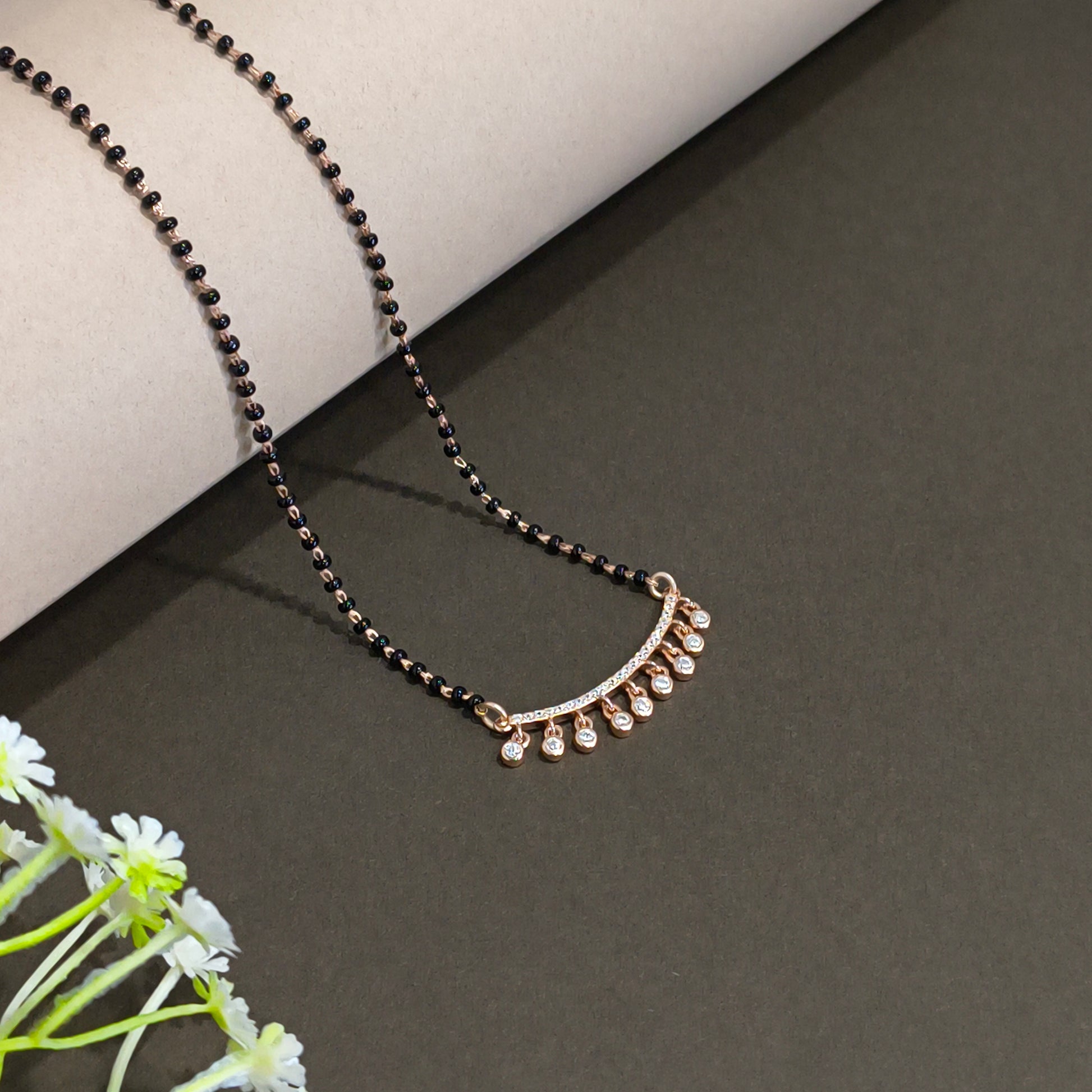 Jewelry with black beads and gold accents on a dark surface with flowers.