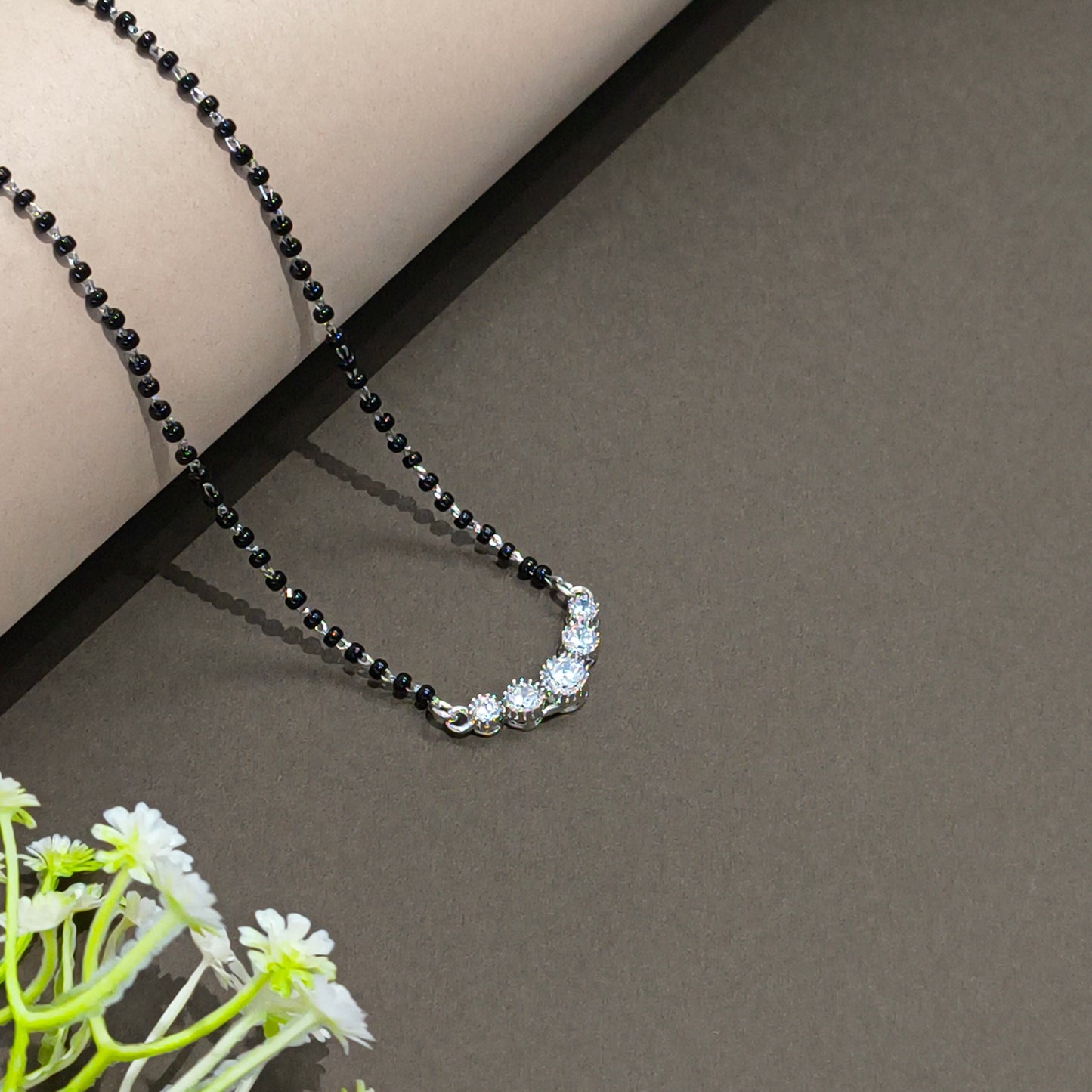 Black beaded necklace on a gray surface with a floral arrangement in the corner