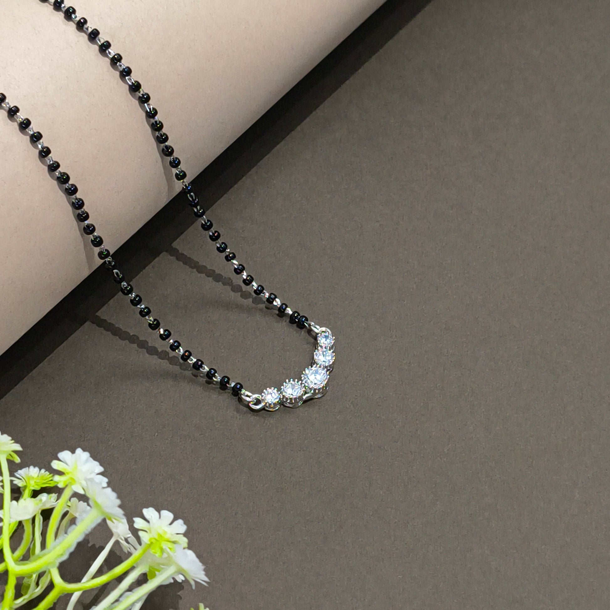 Black beaded necklace on a gray surface with a floral arrangement in the corner