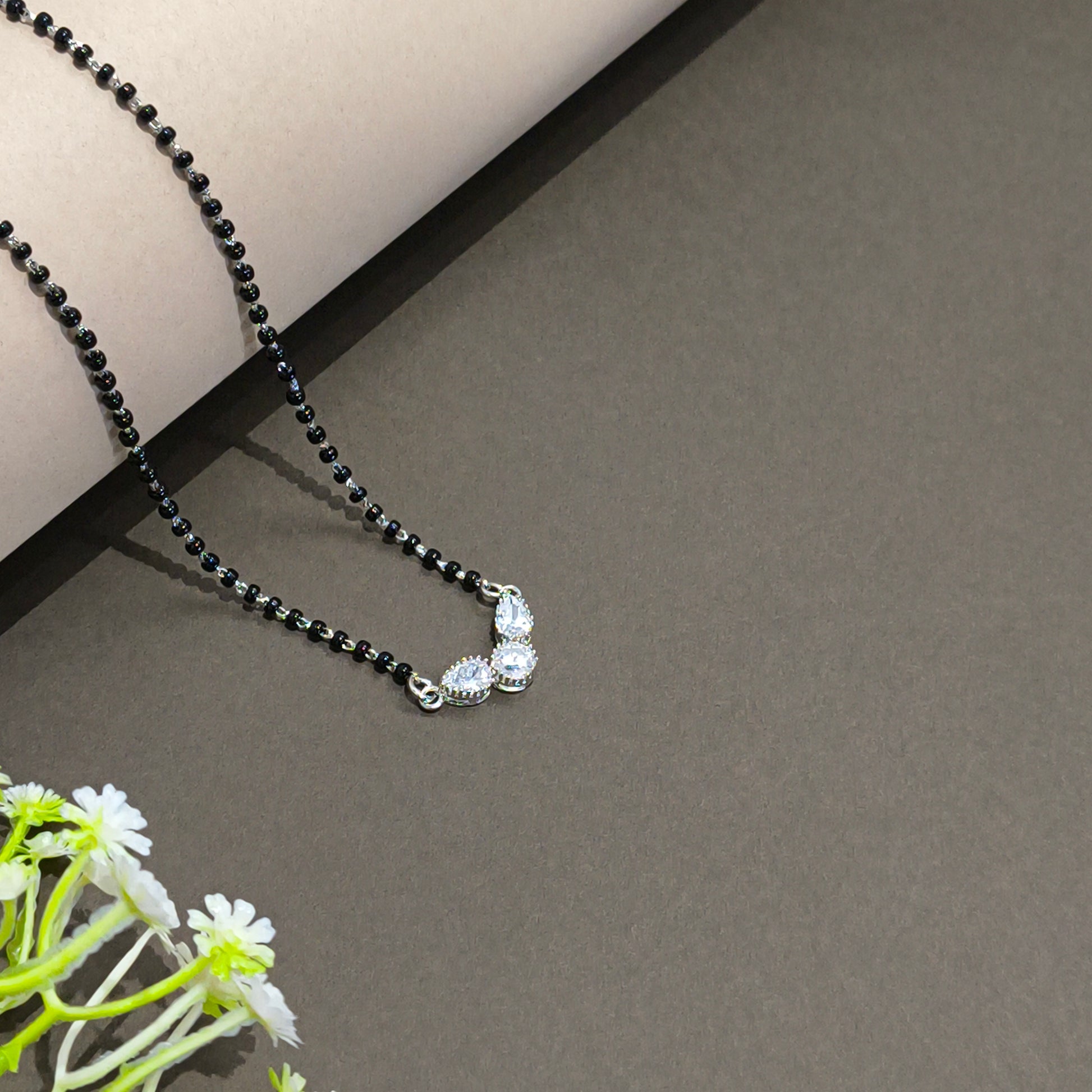 Black beaded necklace with silver clasp on a gray surface with a plant in the corner