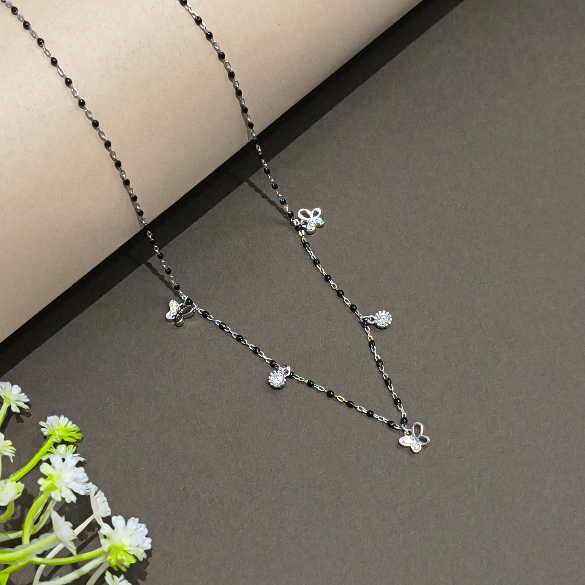 Silver necklace with floral pendants on a gray background with flowers.